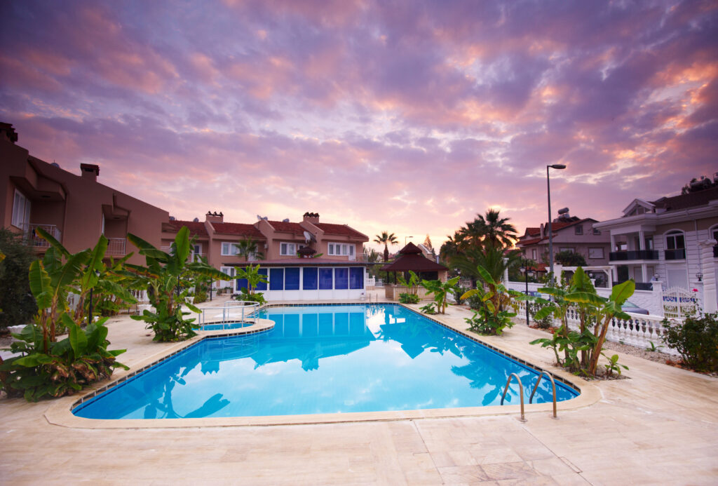 Zwembad bij een luxe halal resort in Turkije, omgeven door villa's en tropische planten onder een kleurrijke zonsondergang.