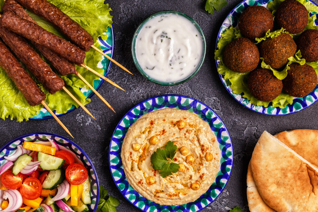 Traditioneel halal Midden-Oosters gerecht met kebabs, falafel, hummus, verse salade en pita broodjes, geserveerd op kleurrijke borden op een donkere stenen ondergrond.