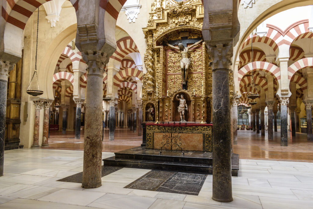 Interieur van de Mezquita in Córdoba, Spanje, met rood-witte bogen, marmeren zuilen en een goud versierd altaar – een historische locatie met islamitisch en christelijk erfgoed.
