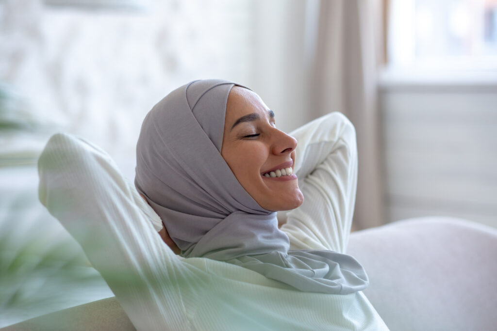 Ontspannen moslima met hoofddoek glimlachend tijdens een rustmoment in een dames-only spa.