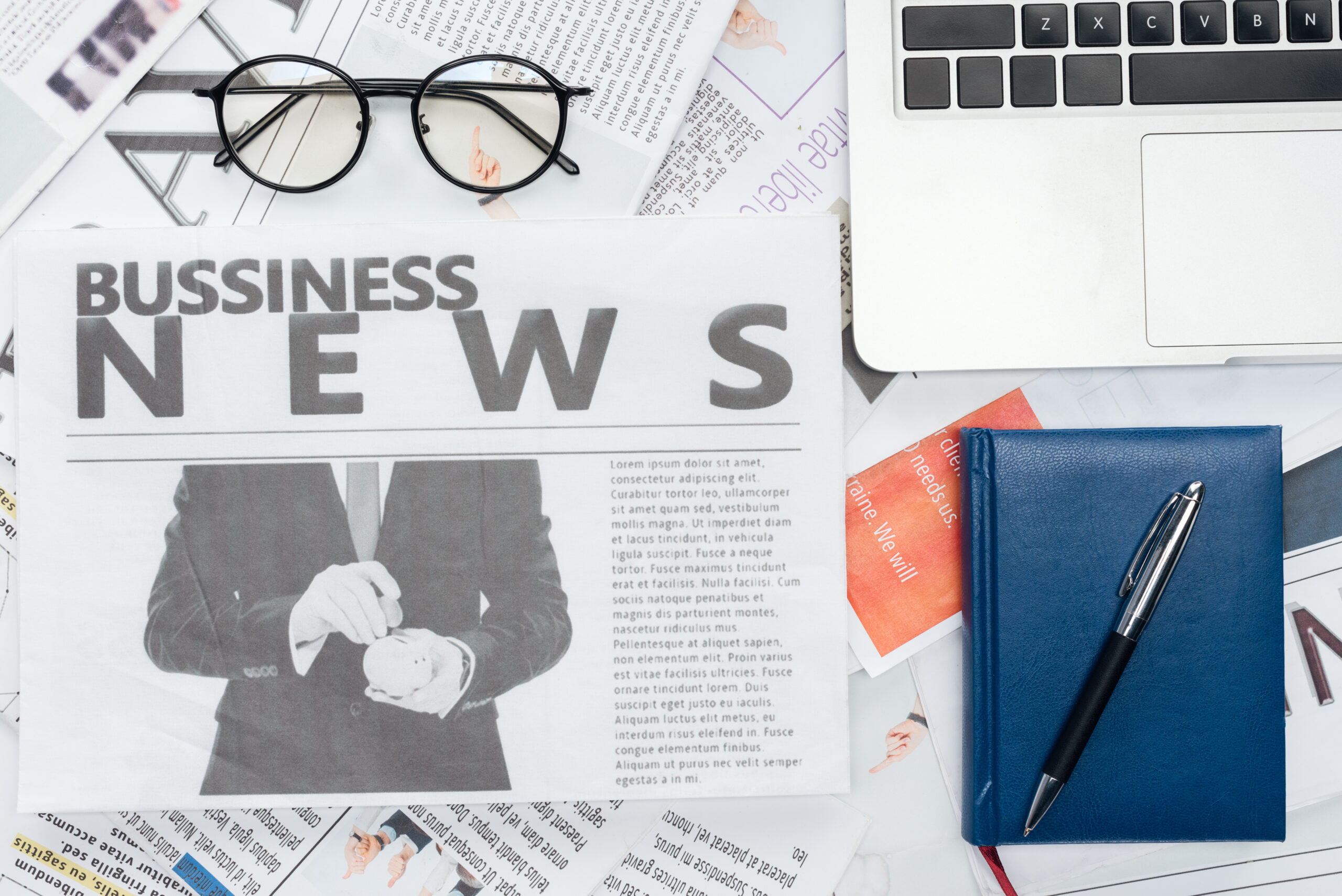 Krant met de kop Business News naast laptop, bril, pen en notitieboek – symbool voor blog en nieuwsartikelen.
