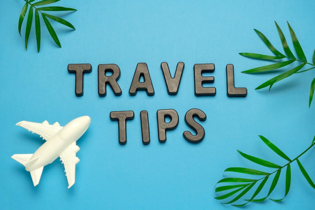 Flat lay afbeelding met de tekst Travel Tips, speelgoedvliegtuig en tropische bladeren op blauwe achtergrond.