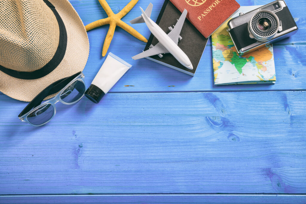 Reisaccessoires met paspoort, vliegtuigmodel, zonnebril, zonnebrandcrème en wereldkaart op blauwe tafel – symbool voor last-minute vakantiedeals.