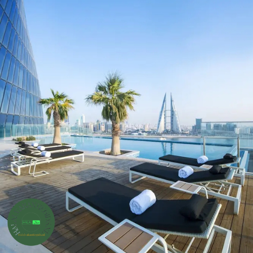 Zonneterras met ligbedden en skyline van Manama bij Wyndham Grand Manama.