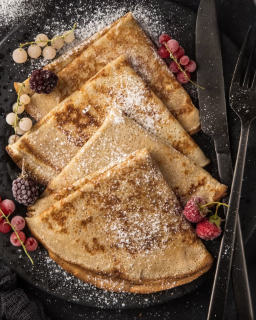 Gevouwen crêpes met poedersuiker, frambozen en bessen op een zwart bord