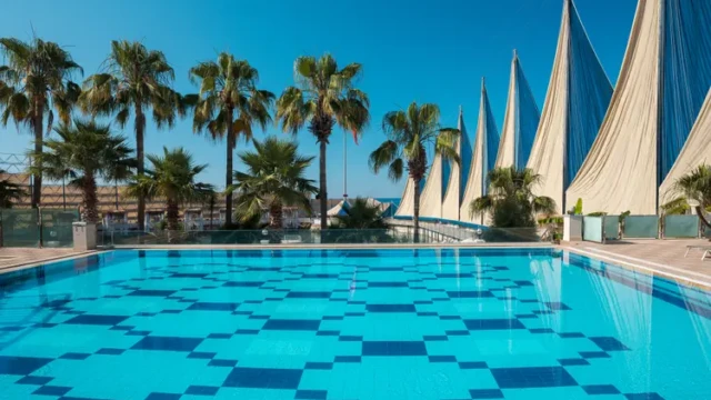 Groot zwembad met zonneterras en privacyvoorzieningen Zwembad van Adin Resort Hotel met palmbomen en afgeschermde omgeving