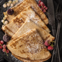 Vers bereide crêpes met poedersuiker en rood fruit bij de AROYA Creperie. Gevouwen crêpes met poedersuiker, frambozen en bessen op een zwart bord