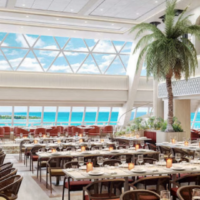 Al Waha Dining combineert een ruime restaurantruimte met veel daglicht en uitzicht op zee. Licht restaurant van Al Waha Dining met gedekte tafels, palmboom en uitzicht op zee
