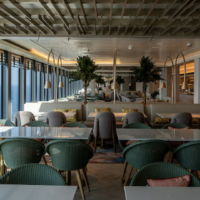 Amwaj Buffet heeft een ruim en modern zitgedeelte met verschillende tafels en comfortabele stoelen. Modern interieur van Amwaj Buffet met groene stoelen, lange tafels en grote ramen