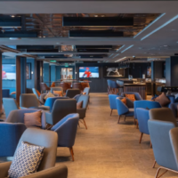 De Legend Lounge biedt comfortabele zitplaatsen in een moderne en ontspannen omgeving. Ruime Legend Lounge met blauwe fauteuils, beeldschermen en een lange bar
