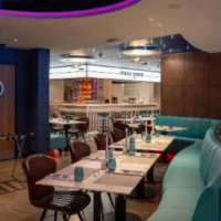 Space Diner heeft een eigentijds dinerinterieur met turquoise zitbanken en opvallende verlichting. Interieur van Space Diner met turquoise banken, gedekte tafels en paarse verlichting