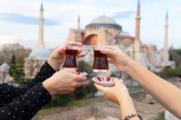 Twee handen die traditionele Turkse thee vasthouden met de Hagia Sophia op de achtergrond in Istanbul.