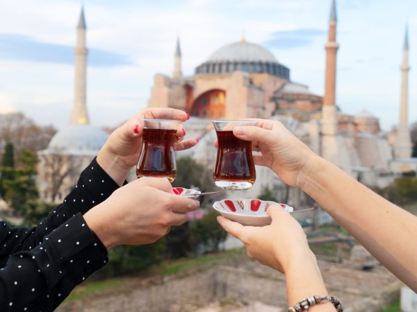 Twee handen die traditionele Turkse thee vasthouden met de Hagia Sophia op de achtergrond in Istanbul.