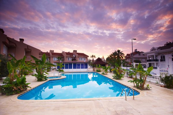 Zwembad bij een luxe halal resort in Turkije, omgeven door villa's en tropische planten onder een kleurrijke zonsondergang.